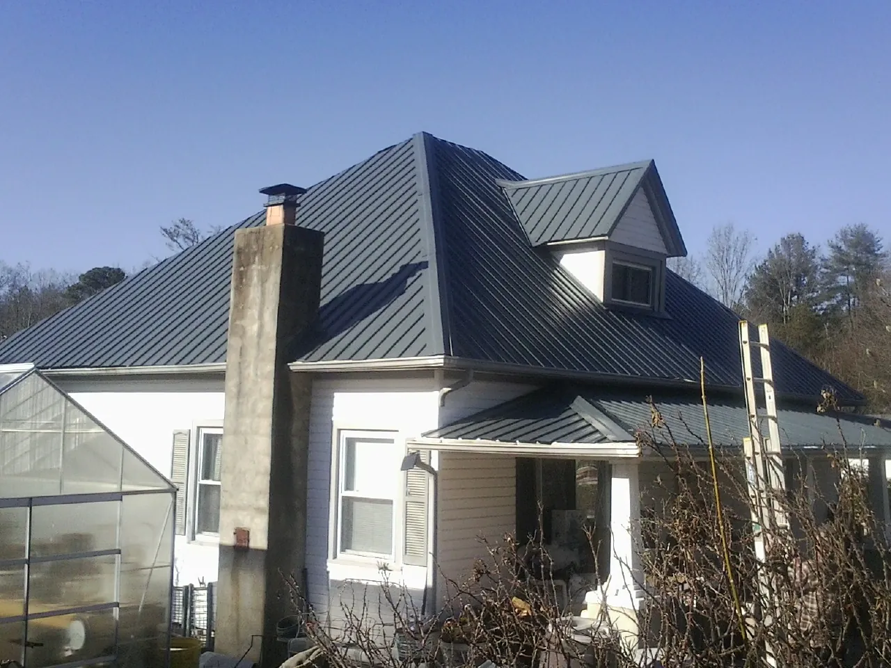 Dark blue standing seam metal roof on a white farmhouse with dormer — Slate & Tile Roof Repair by Roofing Brothers in Derwood