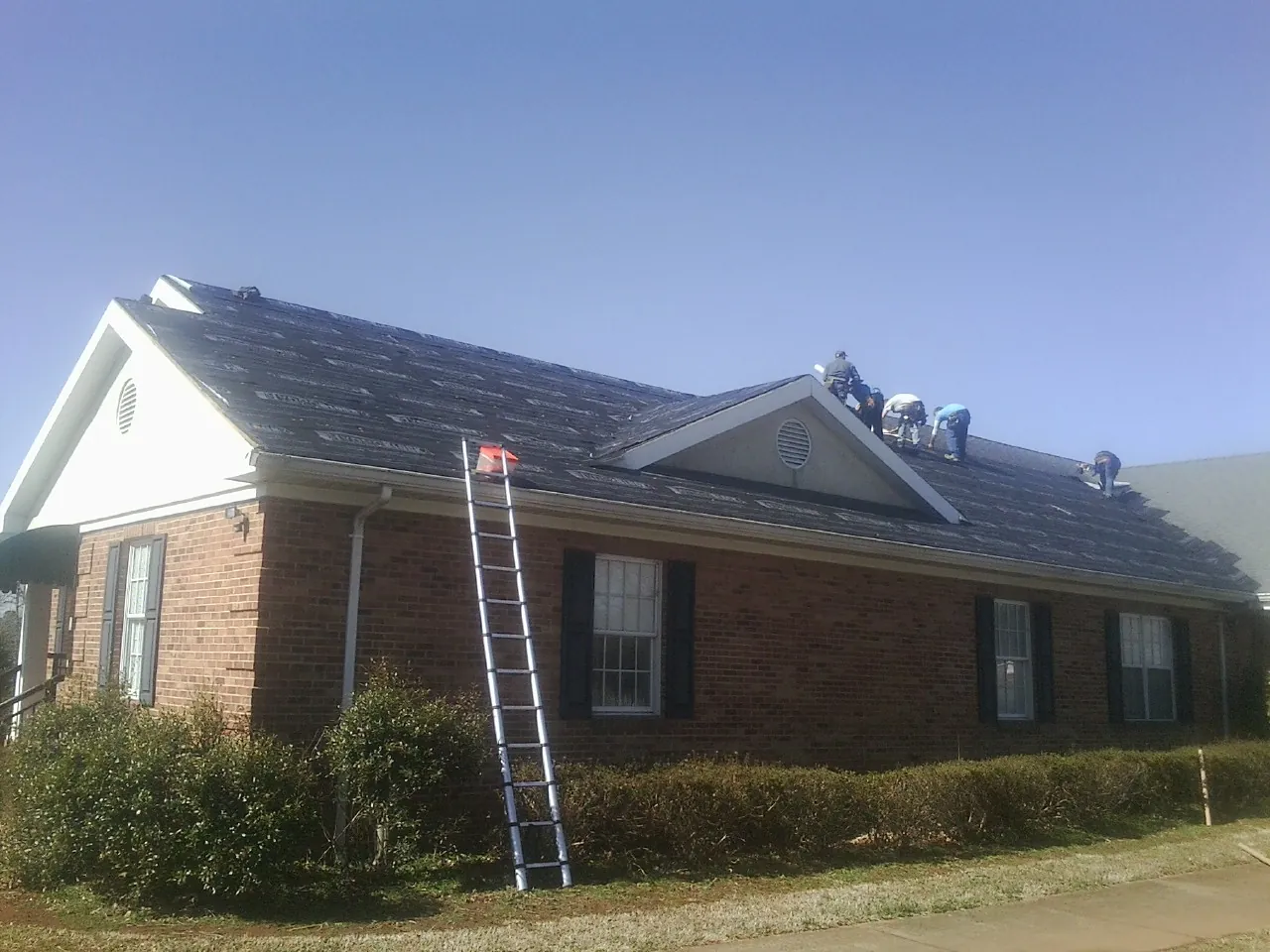 Crew tearing shingles off a brick ranch roof with a ladder set — Metal Roof Repair work by our crew in Derwood