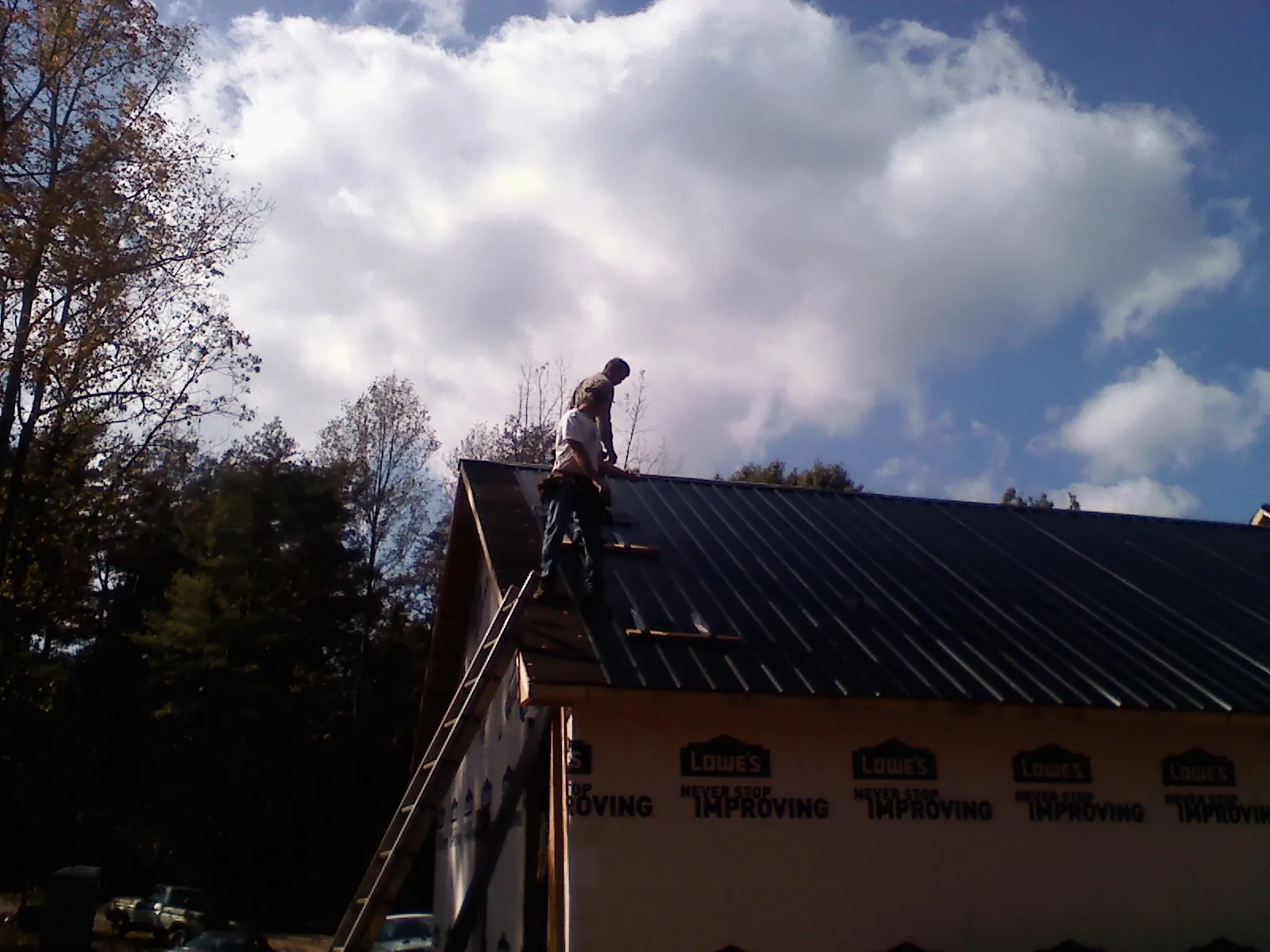 Roofer fastening dark metal panels high against a cloudy sky, from a Roof Inspection job in Derwood