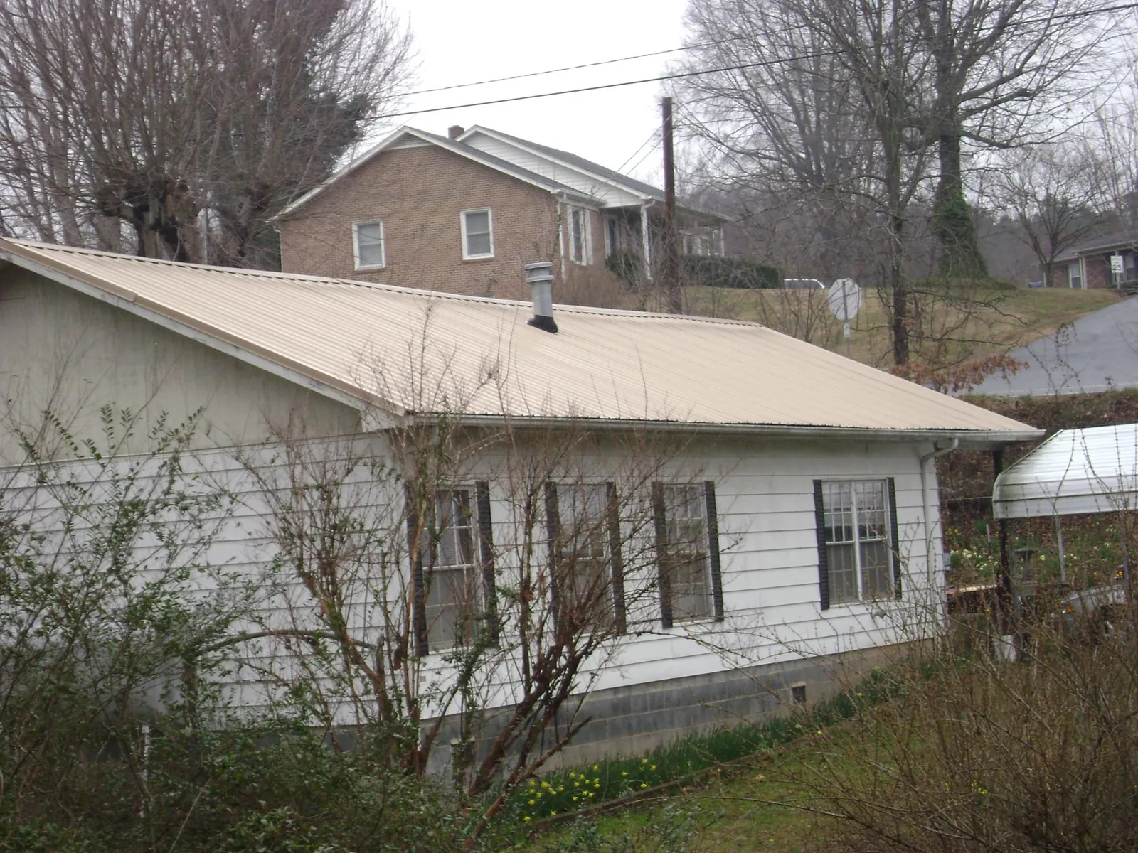 Tan metal roof on a white sided house set into a hillside — Commercial Roofing by Roofing Brothers in Derwood